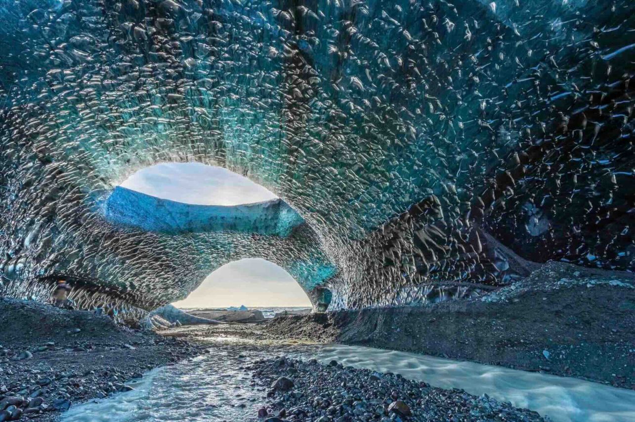 Photographie exposition 2024 Fragilité : intérieur d'une grotte de glace bleue turquoise, tunnel lumineux et fissures dans la glace, fragilité glaciale.