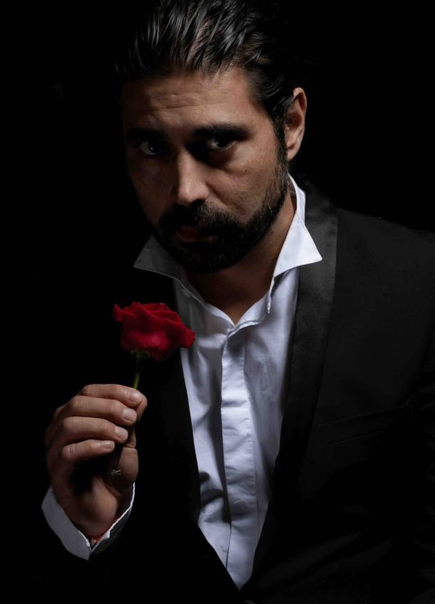 Photographie d'exposition 2025 : homme au regard intense en smoking noir tenant une rose rouge, ambiance dramatique cinématographique.
