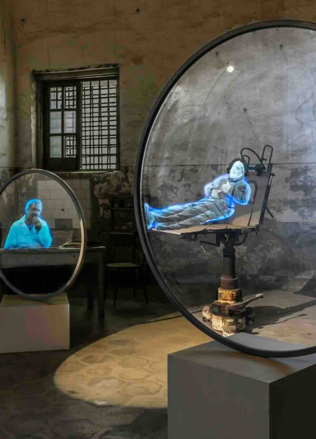 Photographie exposition 2024 Fragilité : hologrammes bleutés de figures humaines dans un ancien laboratoire ou hôpital, technologie éphémère.